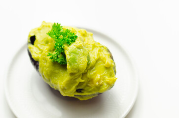 A green avocado with parsley on top sits on a white plate - 776207558