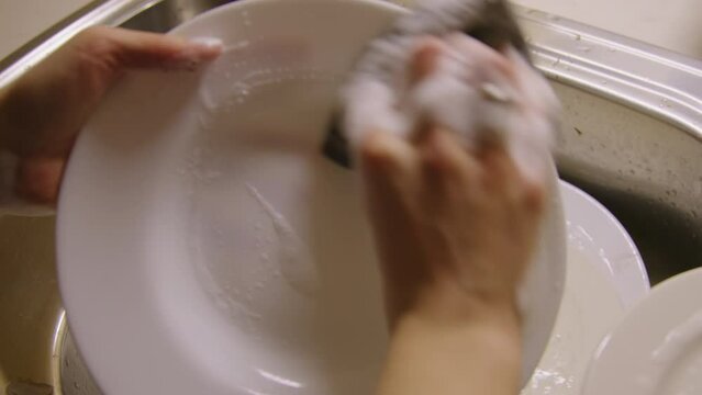At kitchen sink person meticulously washes dishes dishwashing close-up, recognizing vital role of dishwashing in ensuring cleanliness and hygiene for meal preparation and consumption dishwashing.