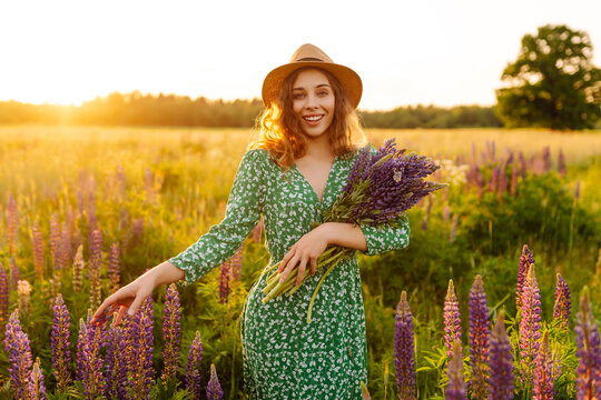 Portrait of young woman holding bouquet of lavender flowers walking in summer meadow. Nature, vacation, relax and lifestyle. Collection of medicinal herbs