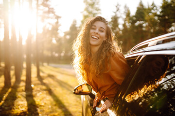 Young woman is resting leaning out of a car window at sunset.  Lifestyle, travel, tourism, nature, active life.