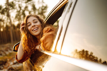 Young woman is resting leaning out of a car window at sunset.  Lifestyle, travel, tourism, nature,...
