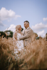 a bride and groom intimately gaze at each other, enveloped by tall wheat in a field, with a cloudy blue sky above them.