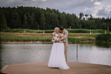 Valmiera, Latvia - Augist 13, 2023 - A bride and groom embrace on a wooden pier by the lake, the...