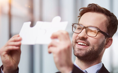 Portrait of optimistic bearded businessman holding puzzle pieces, solving tasks, looking at camera