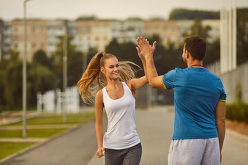 Woman gives a high five to man coach during a workout session in the city park. This portrait...