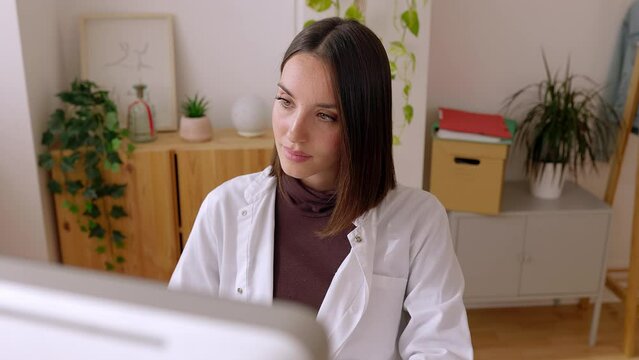 Female doctor in white coat working on laptop at office desk. Professional practitioner woman typing on keyboard looking at computer screen at clinic workplace. Healthcare people concept.