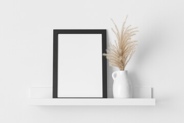 Black frame mockup with a pampas decoration on the wall shelf.
