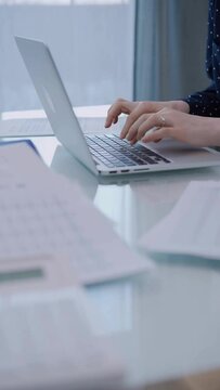 Business woman is working with laptop computer while sitting at the glass table in home office. Female entrepreneur typing information, hands closeup
