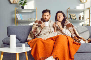 Man and woman are at home in living room, wrapped in warm blanket and feeling flu symptoms.Couple...