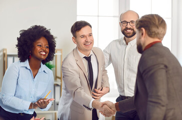 Happy smiling diverse company employees making deal in modern office shaking hands. Business people rejoicing at a successful partnership of colleagues applauding them on a meeting.