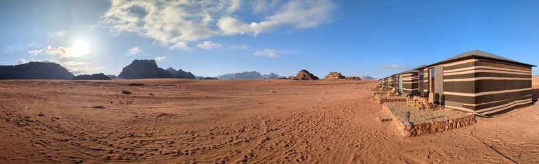 Panorama view of Wadi Rum desert with bedouin tents on flat sand landscape with mountains and rocks...