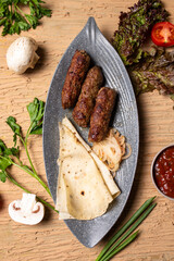 Top view of delicious kebabs lula lamb kebab with grilled vegetables and herbs on a wooden table.