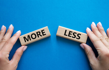 More or Less symbol. Concept word More or Less on wooden blocks. Businessman hand. Beautiful blue background. Business and More or Less concept. Copy space