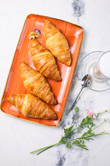 Top view four golden croissants on an orange plate with a cup of coffee on the side