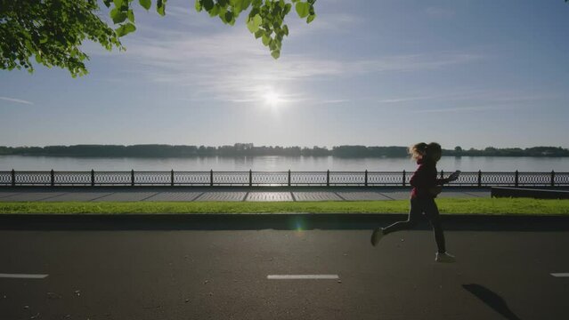 Silhouette of young beautiful girl running or jogging past camera. Woman doing sport or fitness alone in nature. Female exercising at sunset outdoors. Athlete doing exercises for endurance, strength.