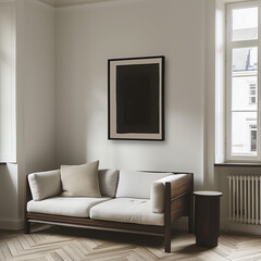 A black framed picture hanging on the wall of an apartment. The sofa is white and beige with wooden legs, next to it there is also a side table. The living room has aherringbone parquet floor