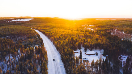 Aerial view from drone of nature landscape capped with snow and surrounded by coniferous forest, bird’s eye view of of snowy trees in national park of north Lapland in winter, road with cars.