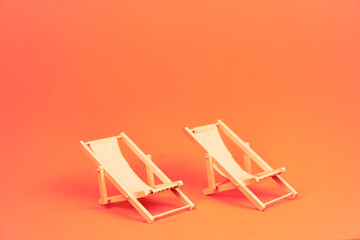 Two miniature beach loungers on orange background. Summer vacation, relaxation concept - obrazy, fototapety, plakaty
