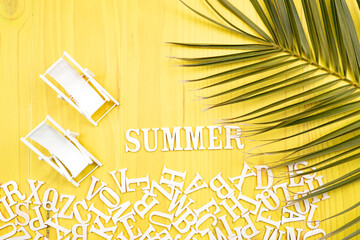 Top view composition viewed from above with letters of the alphabet accumulated at the bottom forming the word Summer with two miniature beach loungers on yellow background.
