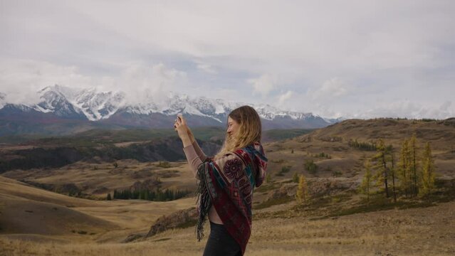Woman taking pictures of nature, selfies. Young girl against of snow-capped mountains, yellow nature, hills and plains making photos as souvenir. Travel, tourism, hiking, new experiences, expressions.