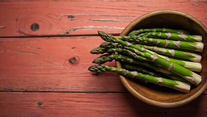 Organic green asparagus spears arranged neatly in a rustic wooden bowl, on a red wooden table surface