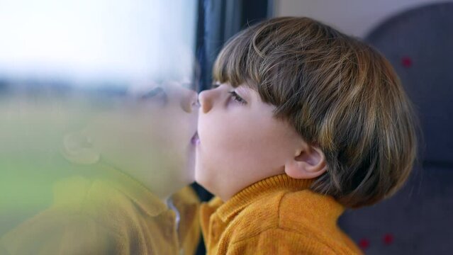 Bored funny small boy with face glued on trian window. Mouth and lips pressed on glass and staring at landscape scenery pass by in transportation
