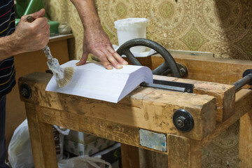 Older man's hands gluing sheets of paper on antique work table