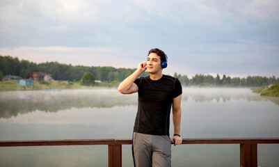 Portrait of handsome sporty man wearing headphones and listening to music after jogging on the nature. Relaxation and resting concept