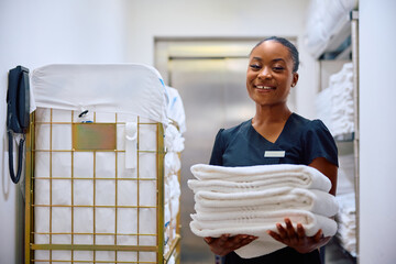Happy black chambermaid working in  hotel and looking at camera. - obrazy, fototapety, plakaty