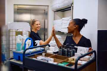 Happy chambermaids giving high-five while working in hotel.