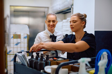 Young hotel maid and housekeeping manager checking cleaning trolley supplies.