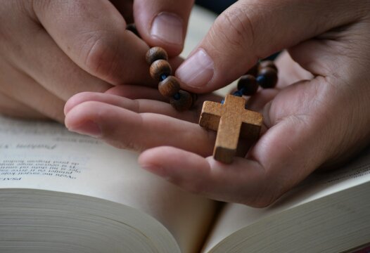 Man pray on Holy Bible and holding wooden rosary