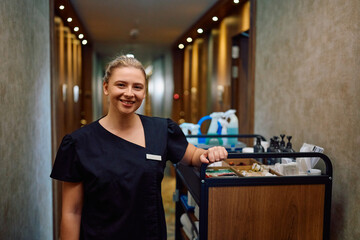 Happy chambermaid cleaning rooms in hotel and looking at camera.