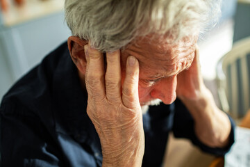 Distressed senior man holding head in hands at home