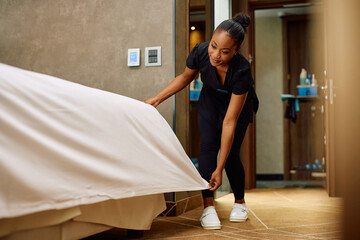 African American hotel maid making bed in guest's room. - obrazy, fototapety, plakaty