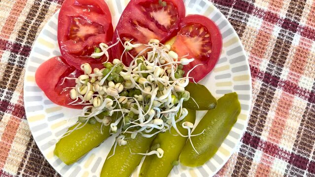 Salad of fresh vegetables and micro-greenery. Tomatoes, apples, pickles, finely chopped, a mound of sprouted mung beans on a white plate on a colored background. Close-up