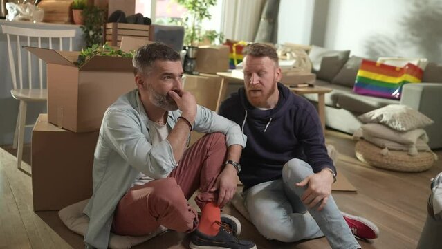 Male gay couple making plans in new home after moving in