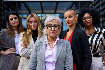 Group of multiracial and diverse ages business only women standing in formal suit conditioning their clothes while looking at camera outdoor. Serious, empowered, successful, professional female worker
