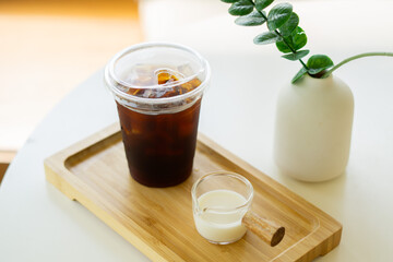 Glass of ice coffee and milk with white flower and leaf in white vase on white table at cafe.
