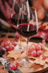 Autumn still life with two glasses of red wine, grapes and dry leaves in rustic style on dark wooden background. Romantic sweater weather concept with copy space