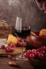 Glass of red wine served with blue cheese on dark wooden background. Autumn picnic with wine and cheese platter, fruits and dry leaves in rustic style
