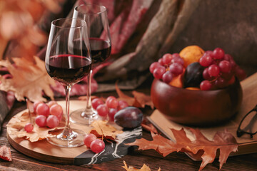 Naklejka na ściany i meble Autumn still life with two glasses of red wine, grapes, book and dry leaves in rustic style on dark wooden background. Romantic sweater weather concept with copy space