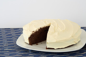 Round dark chocolate cake with  delicate white frosting, with a slice taken out.