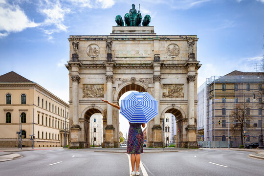 Munich travel concept with a tourist woman holding an umbrella in front of the Victory Gate, Germany