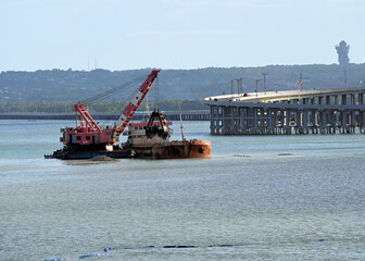 Dredging Operation in Ocean with Nearby Raised Highway and Mountains in Background with Statue in Bali Indonesia