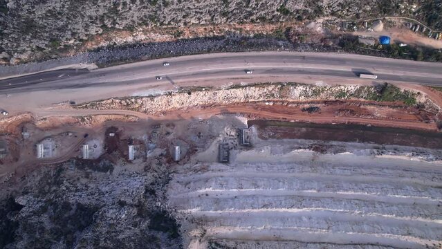 Aerial view of highway ledges under construction after drilling and blasting operations. Road construction at rough highland terrain. Supports of bridge overpass under construction top down aerial 