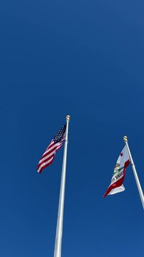 USA and California flags waiving in the wind against blue sky