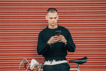 young man with mobile phone and bicycle on the street in red background