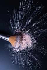 Make up brush sitting in makeup powder in studio on a black background