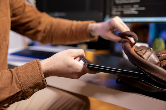 Programmer putting laptop in backpack, leaving office after filtering malicious traffic from cybercriminals attempting to steal company data. Man packing notebook after finishing preventing malware